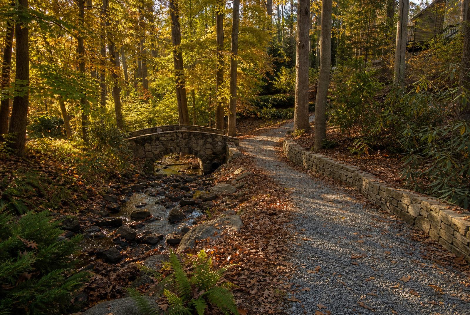 Private walking trail and arched stone bridge through autumn hardwoods